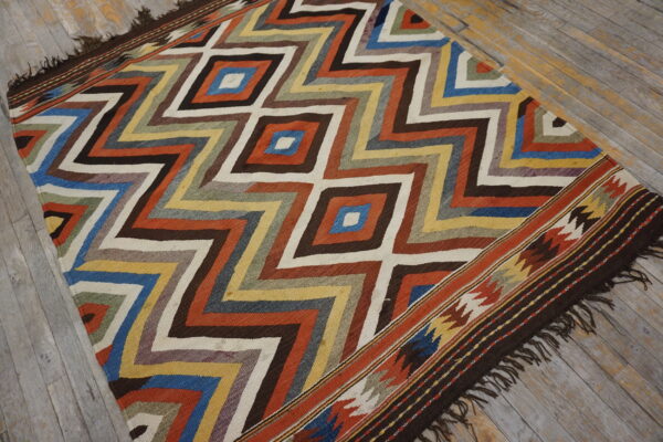 Colorful flatwoven rug featuring complex diamond and zigzag patterns displayed on rustic hardwood flooring.