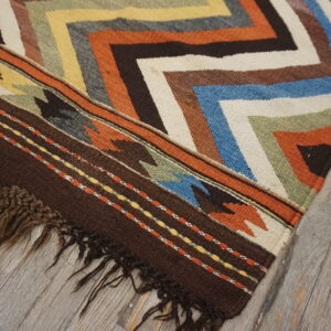 Multicolor flatweave rug with chevron patterns and dark brown fringe on weathered gray wood floor.