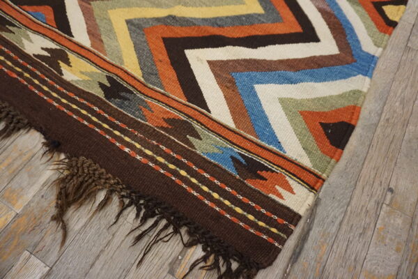 Multicolor flatweave rug with chevron patterns and dark brown fringe on weathered gray wood floor.