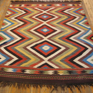 Flatweave rug with a central multicolored diamond and chevron pattern rests on light wood floors.