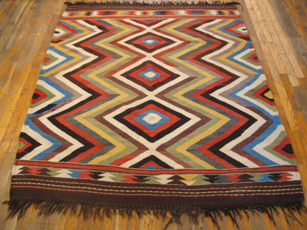 Flatweave rug with a central multicolored diamond and chevron pattern rests on light wood floors.