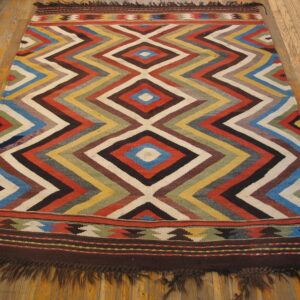 Low pile rug featuring a multi-colored zigzag diamond pattern and fringed borders on wood planks.