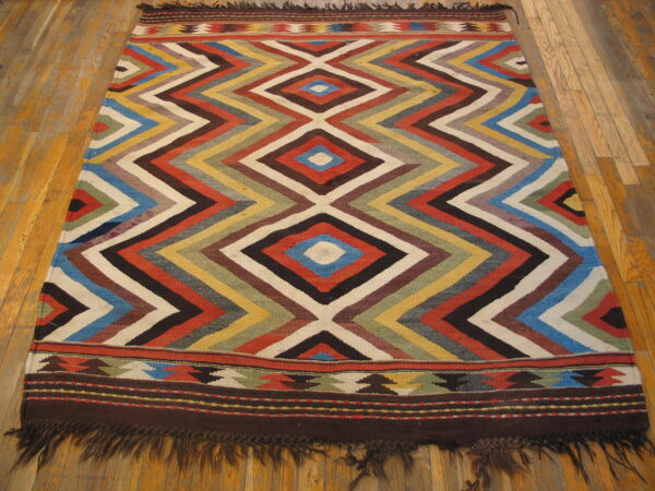 Low pile rug featuring a multi-colored zigzag diamond pattern and fringed borders on wood planks.