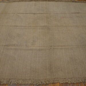 Neutral khaki flatweave rug with subtle vertical texture stripes and thick fringe on wooden floorboards.