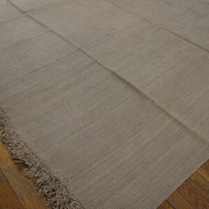 Muted beige flat-woven rug displaying stitched panel construction and fringe on rustic hardwood floors.