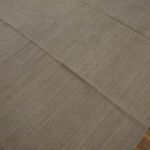 Solid light brown flatweave rug constructed from visible stitched panels covers hardwood flooring.