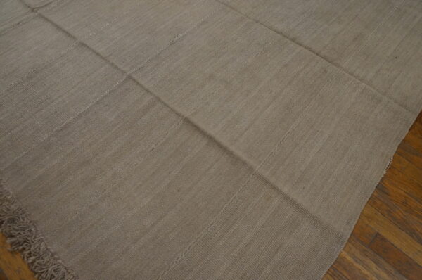 Solid light brown flatweave rug constructed from visible stitched panels covers hardwood flooring.