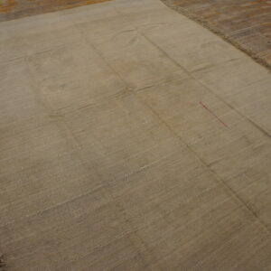 Large tan flat-weave rug showing panel seams and fringe rests on a wood floor.