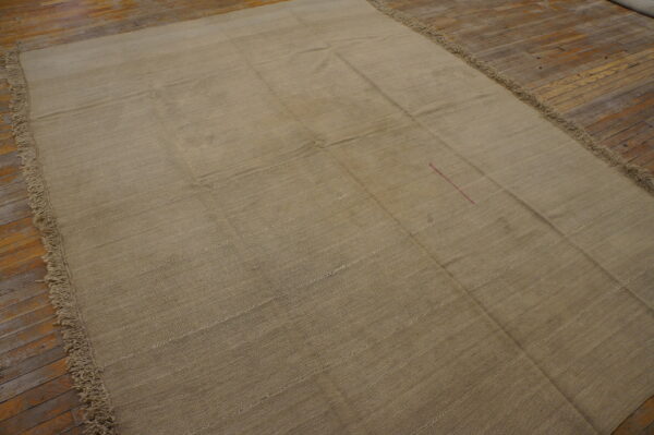 Large tan flat-weave rug showing panel seams and fringe rests on a wood floor.