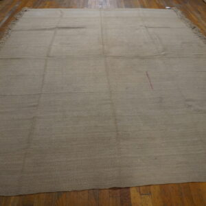 A large neutral tan rug with horizontal texture and pink marking lies on distressed wood floors.