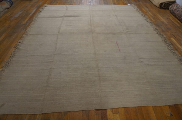 A large neutral tan rug with horizontal texture and pink marking lies on distressed wood floors.