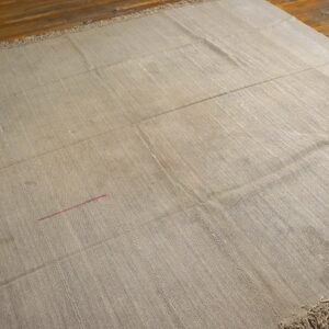Textured tan rug made of stitched panels, showing fringe and a pink thread detail on wood floors.