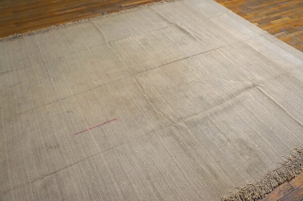 Textured tan rug made of stitched panels, showing fringe and a pink thread detail on wood floors.