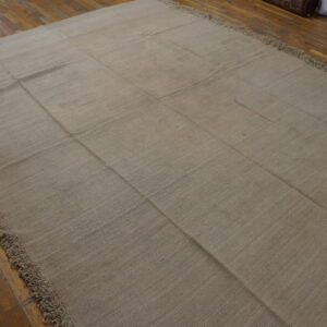 A large, beige flatweave rug with visible seams creating a grid pattern rests on distressed hardwood flooring.