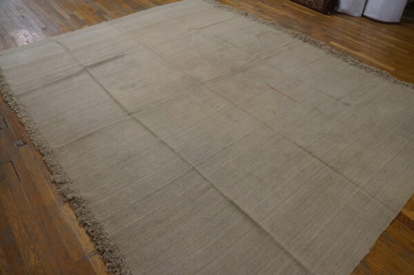 A large, beige flatweave rug with visible seams creating a grid pattern rests on distressed hardwood flooring.