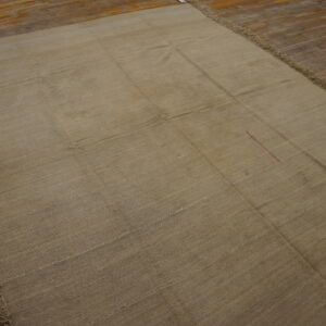 Khaki flat-woven rug with sewn grid seams and long fringe lies on distressed wood plank flooring.