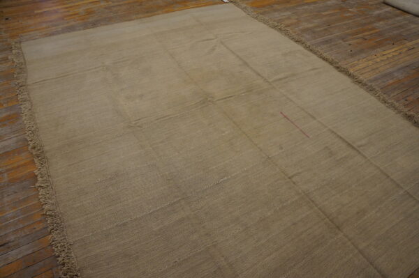 Khaki flat-woven rug with sewn grid seams and long fringe lies on distressed wood plank flooring.