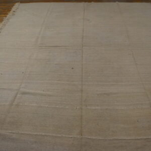 Solid beige flatweave rug featuring visible horizontal seams and fringed edges on distressed wood floors.