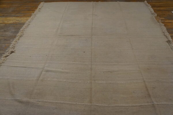 Solid beige flatweave rug featuring visible horizontal seams and fringed edges on distressed wood floors.