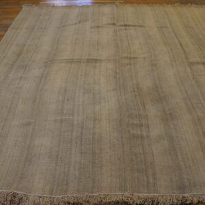Large neutral woven rug with vertical texture and fringes covering a dark wood floor.