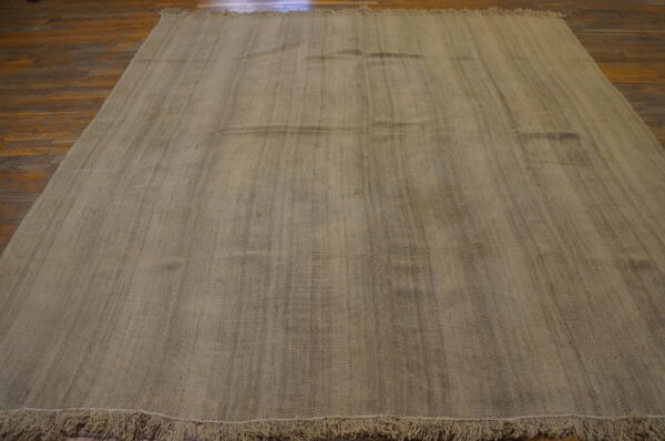Large neutral woven rug with vertical texture and fringes covering a dark wood floor.