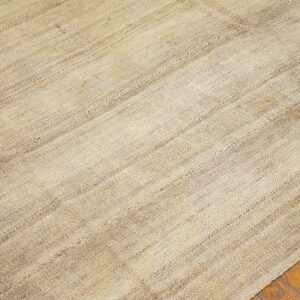 Natural toned, flatwoven rug with patched seams and textured stripes rests on rustic wood flooring.