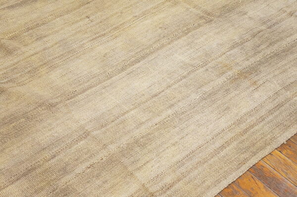 Natural toned, flatwoven rug with patched seams and textured stripes rests on rustic wood flooring.
