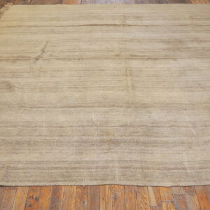Neutral flatweave rug with subtle horizontal stripes and fringes on a distressed wood plank floor.