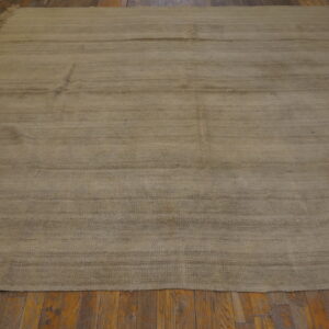 A large neutral tan flatweave rug with short fringe and horizontal striations rests on a rustic wood floor.