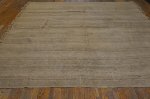 A large neutral tan flatweave rug with short fringe and horizontal striations rests on a rustic wood floor.