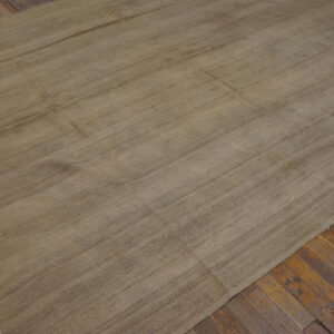 A large, beige flatweave rug with striations rests on rustic wooden floorboards.