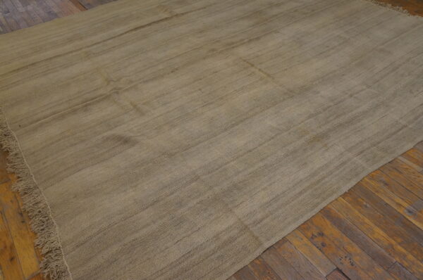 A large, beige flatweave rug with striations rests on rustic wooden floorboards.