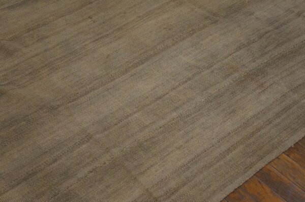 A mottled brown and gray flatweave rug with horizontal seams is laid over dark hardwood floors.