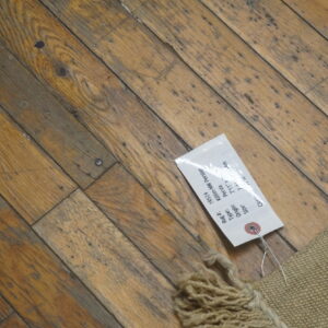 Low-profile tan rug with chunky fringe detail rests on distressed diagonal hardwood flooring.