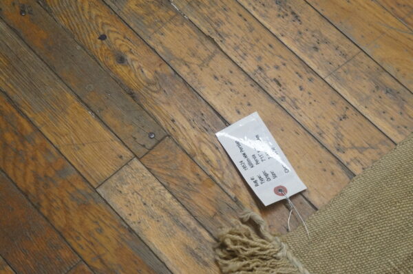 Low-profile tan rug with chunky fringe detail rests on distressed diagonal hardwood flooring.