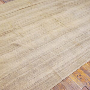 Light beige flatweave rug with textured striations and fringe covering distressed wood plank flooring.