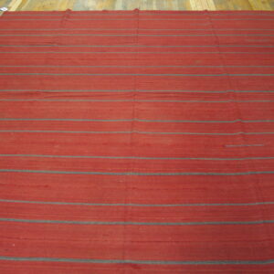 A large, flatweave red rug with thin gray horizontal stripes covers a light brown wood floor.