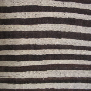 Flatweave rug with thick horizontal stripes of dark brown and cream beside wood flooring.