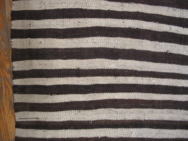Flatweave rug with thick horizontal stripes of dark brown and cream beside wood flooring.