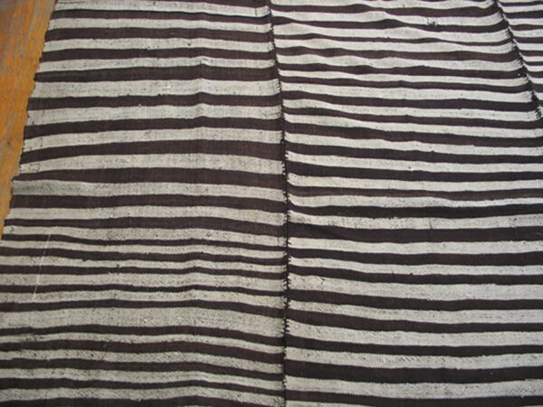 Brown and white striped rug composed of two vertical panels joined by stitching, resting on a wood floor.