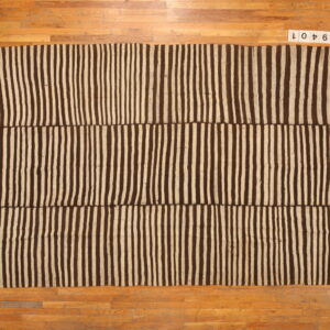 Flatwoven rug featuring wide vertical stripes in dark brown and tan, displayed on a wooden floor.