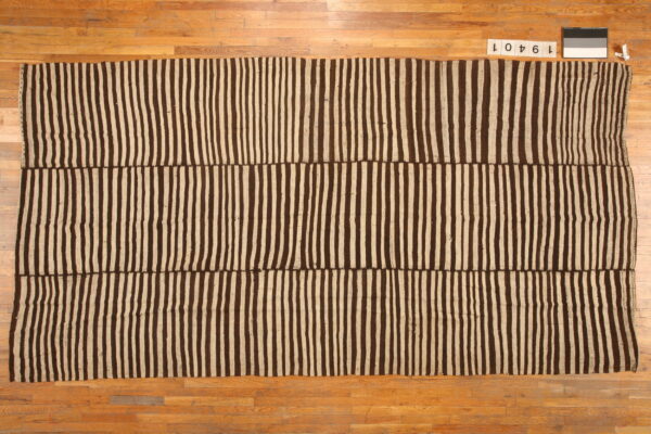 Flatwoven rug featuring wide vertical stripes in dark brown and tan, displayed on a wooden floor.