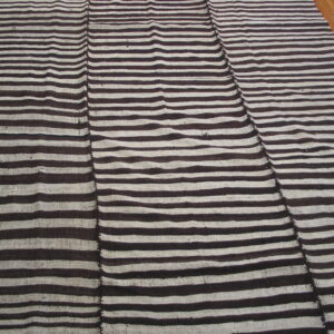 Flatweave rug with dark brown and beige horizontal stripes, visibly stitched together in vertical panels on wood flooring.