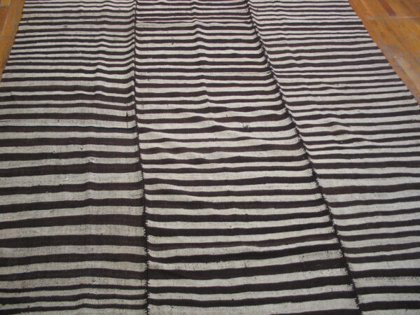 Flatweave rug with dark brown and beige horizontal stripes, visibly stitched together in vertical panels on wood flooring.