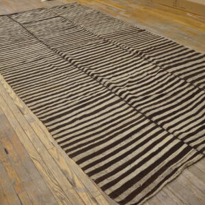 Textured flat-weave rug featuring wide brown and beige stripes displayed on rustic wood planks.