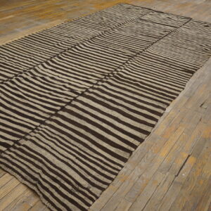 Dark brown and beige striped flat-weave rug displayed on distressed, light brown wooden planks.