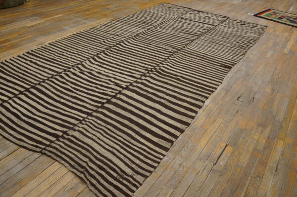 Dark brown and beige striped flat-weave rug displayed on distressed, light brown wooden planks.