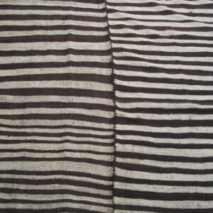 Flat-woven rug with dark brown and cream horizontal stripes, showing a vertical seam, resting on wood floor.