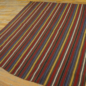 Flatwoven rug featuring thin vertical stripes of red, blue, yellow, and white on wide wooden planks.