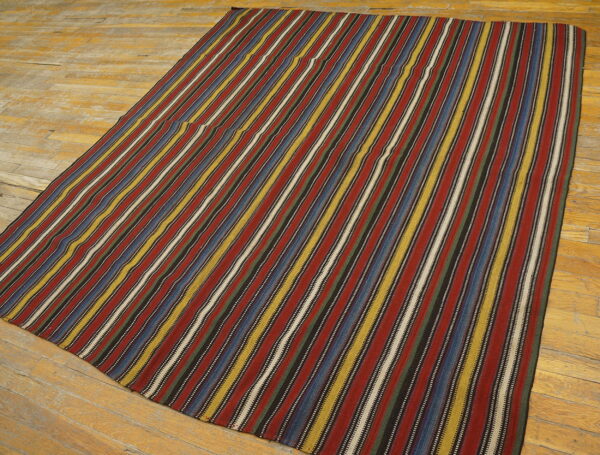 Flatwoven rug featuring thin vertical stripes of red, blue, yellow, and white on wide wooden planks.